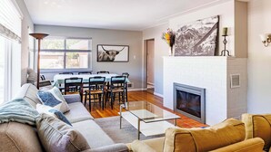 A modern living room with a sofa, a glass coffee table, a fireplace, and a dining area with chairs and a table.