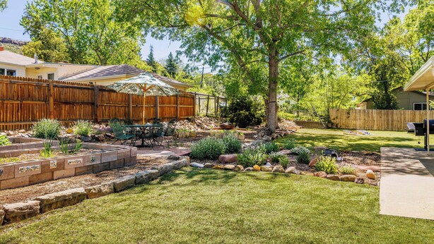 A backyard with a wooden fence, a tree, and a patio area with a table and chairs.