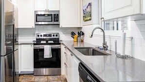A modern kitchen with white cabinets, stainless steel appliances, a granite countertop, and a dishwasher.