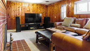 A cozy living room with wooden paneling, a leather sofa, a flat-screen TV, and a fireplace.