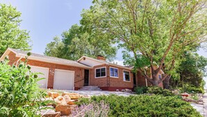 A brick house with a garage, surrounded by greenery and trees.