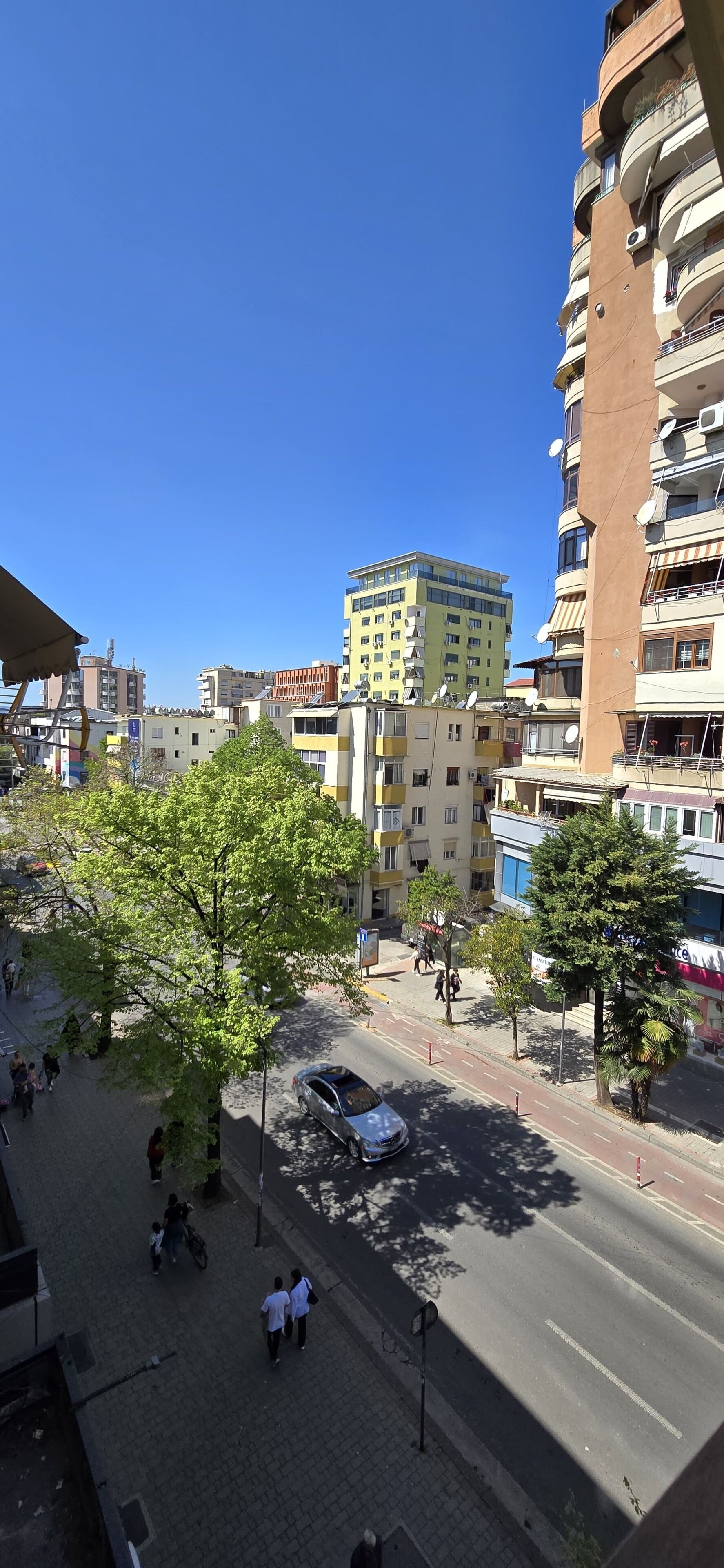 A multi-story building with balconies and satellite dishes, surrounded by trees and a clear blue sky.