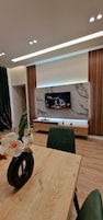 Una habitación moderna con una mesa de comedor de madera, sillas verdes, un televisor montado en una pared de mármol y un mueble de madera debajo.