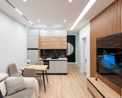 Una cocina moderna con una isla central, un área de comedor con sofá y sillas, y un televisor instalado en una pared de paneles de madera.