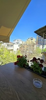 Un balcón con vistas a edificios urbanos, una mesa de madera y flores rojas.