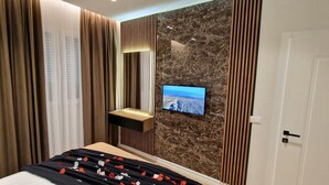 A modern hotel room with a bed, a TV mounted on a marble wall, and a bedside table with a lamp.