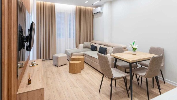 A modern living room with a sofa, a dining table with chairs, a wooden coffee table, and a TV mounted on the wall.