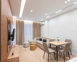 Una sala de estar moderna con un sofá, una mesa de comedor con sillas, una mesa de centro de madera y un televisor montado en la pared.