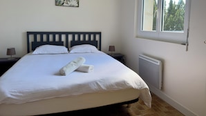 A bedroom with a large bed, two bedside tables, a window, and a radiator. - Panoramic Chalet (Cenves)