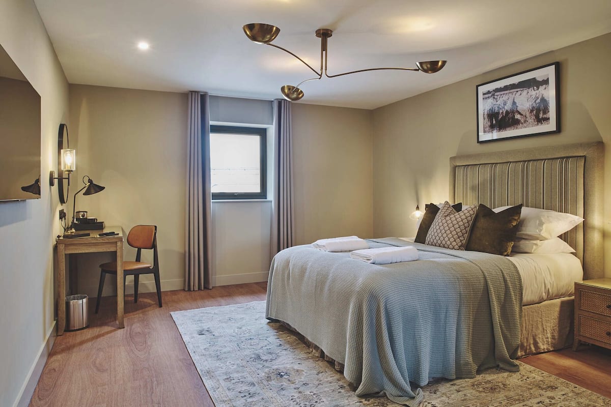 Ein Schlafzimmer mit Bett, Nachttisch, Lampe, Stuhl und Fenster.
