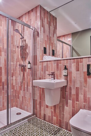 A modern bathroom with a glass shower enclosure, a white sink, and a toilet. - The Barn Hotel (Solihull)