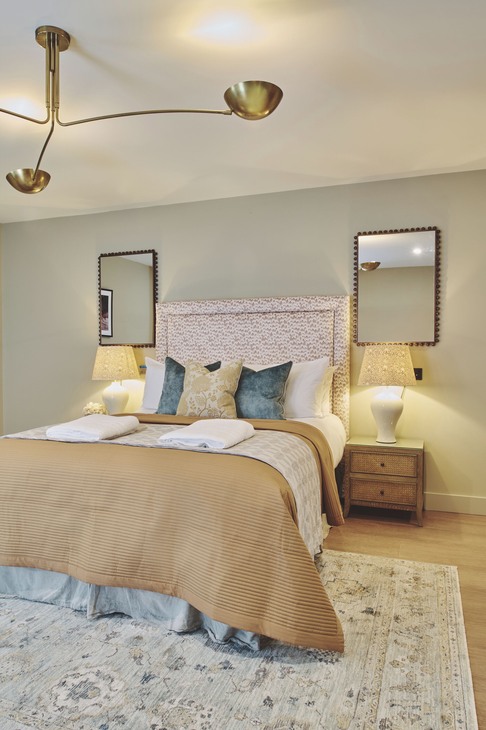 A neatly arranged bedroom with a large bed, two bedside tables with lamps, a ceiling light fixture, and two wall-mounted mirrors.