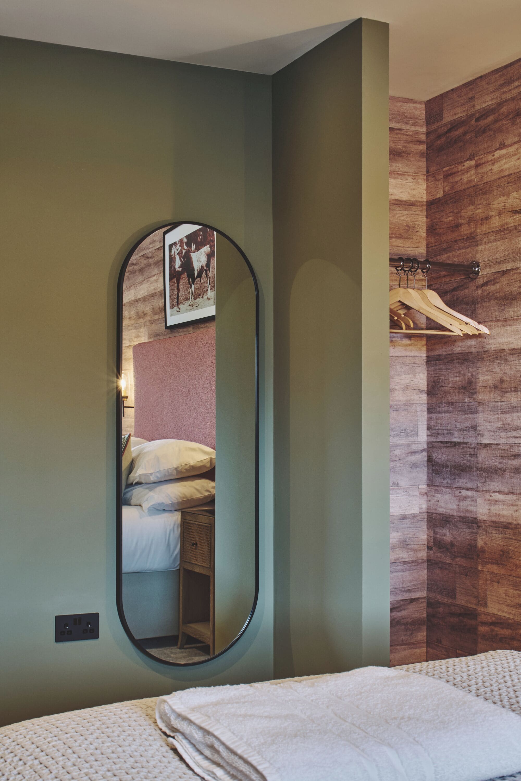 A bedroom with a bed, a mirror, a wooden wall, and a hanging rack.