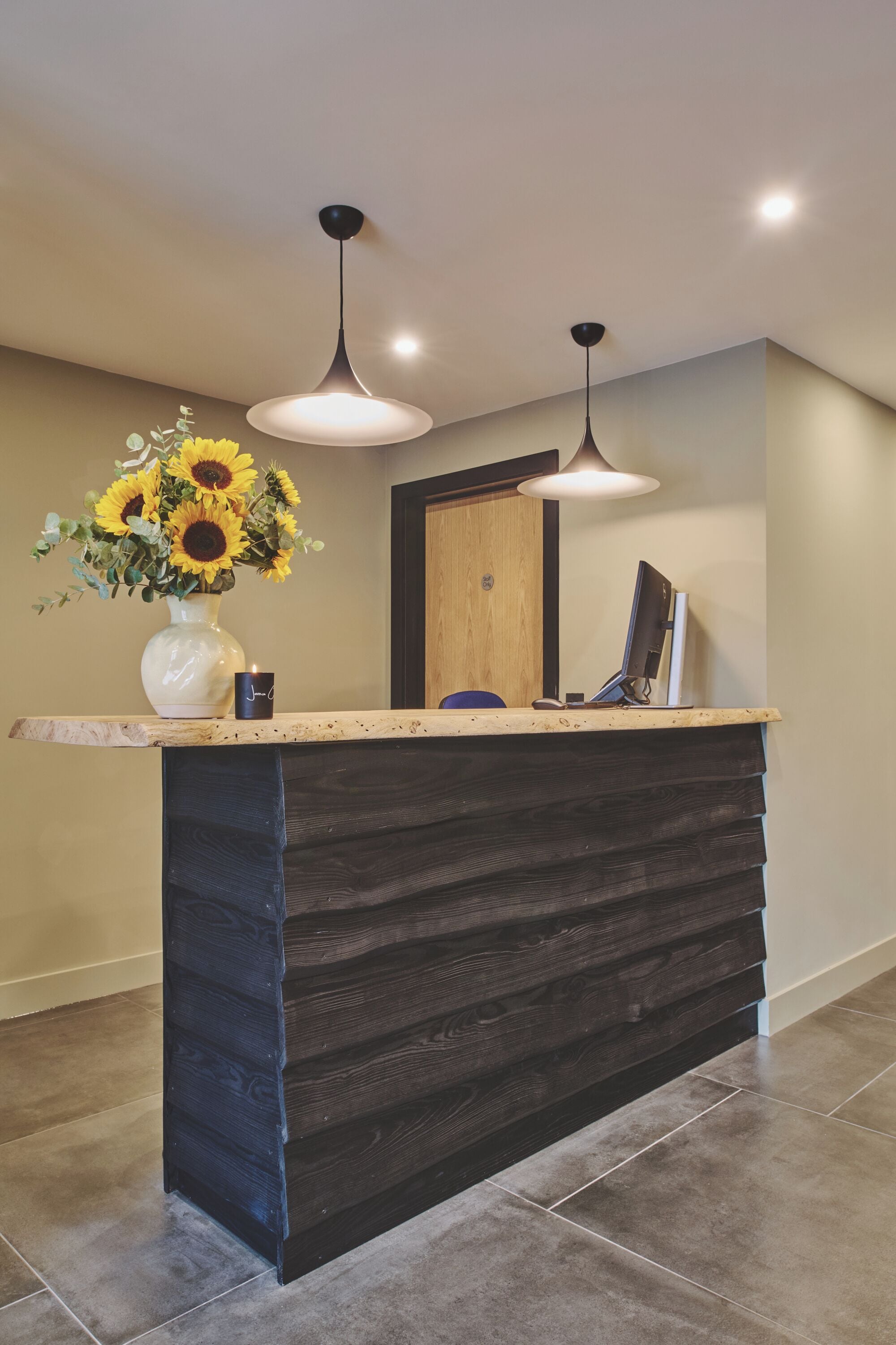 A reception desk with a vase of sunflowers, a candle, and a computer monitor.