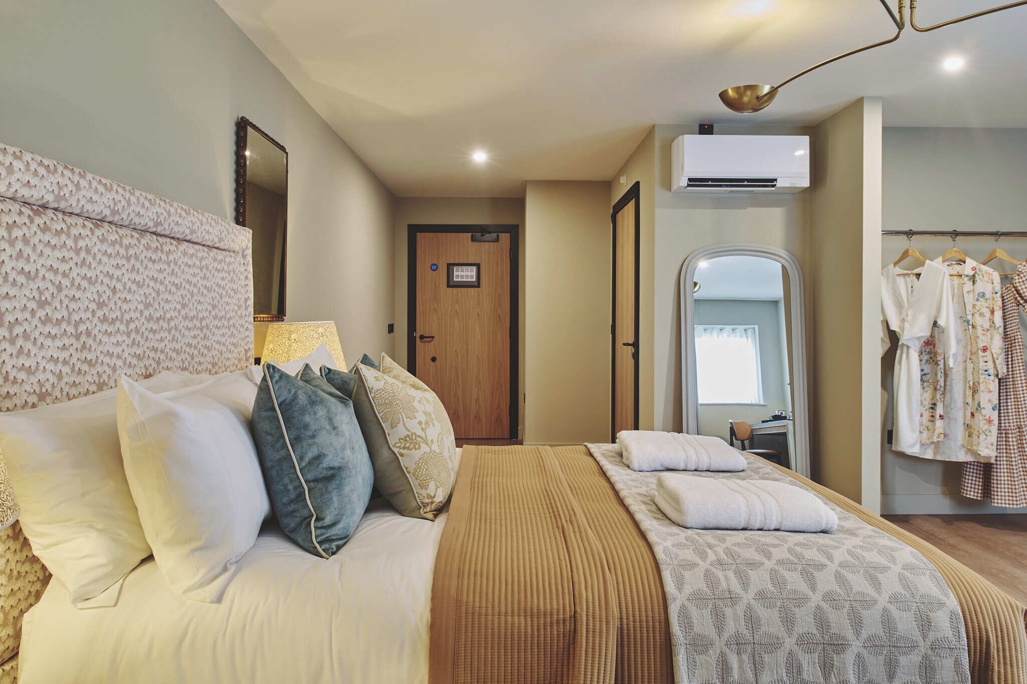 Un dormitorio ordenado con una cama grande, una mesita de noche, un espejo y un perchero.