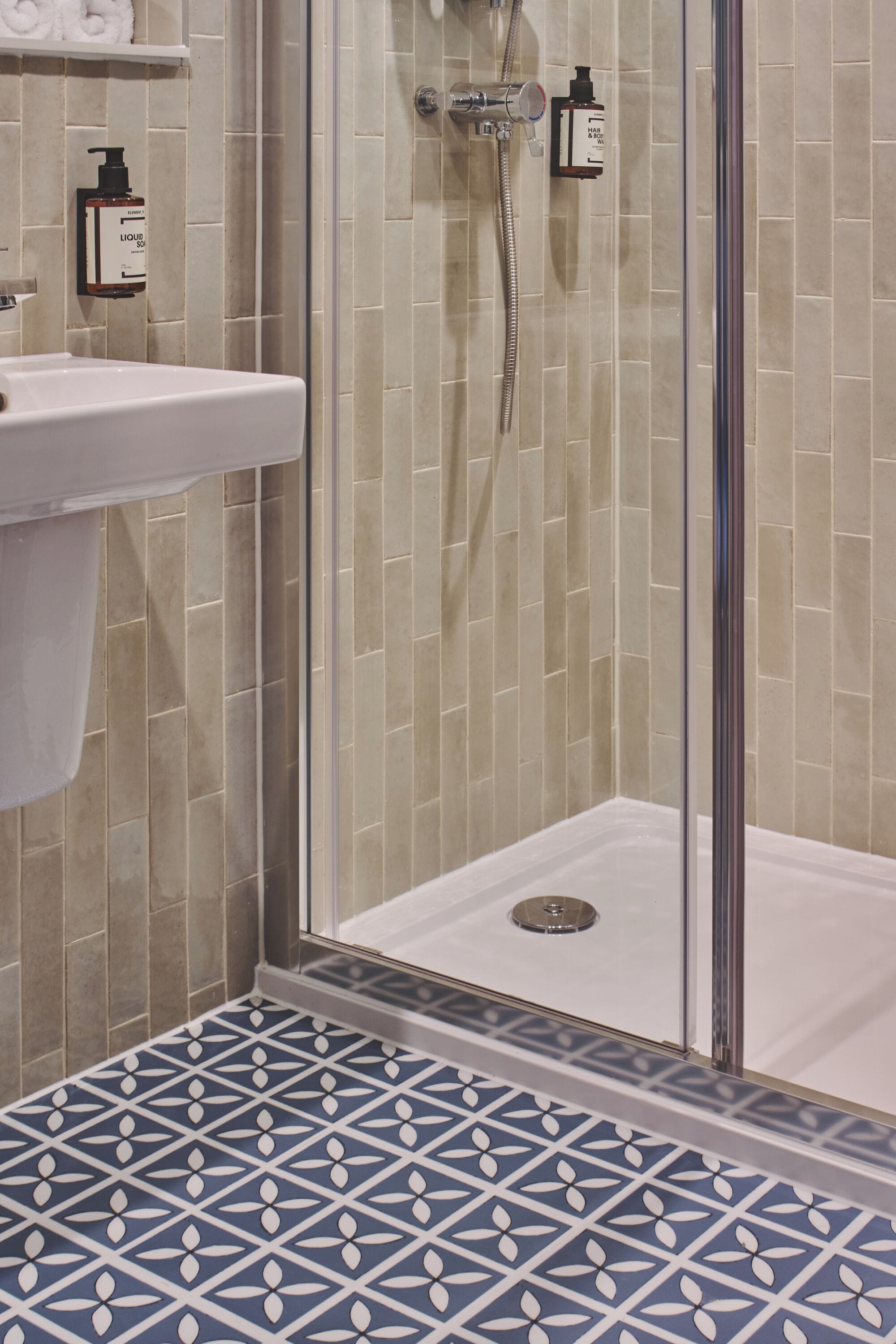 Un baño con ducha, lavabo y azulejos con diseño.