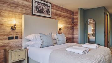 Ein ordentlich eingerichtetes Schlafzimmer mit einem großen Bett, zwei Wandlampen, einem gerahmten Bild über dem Bett und einem Spiegel an der Wand.