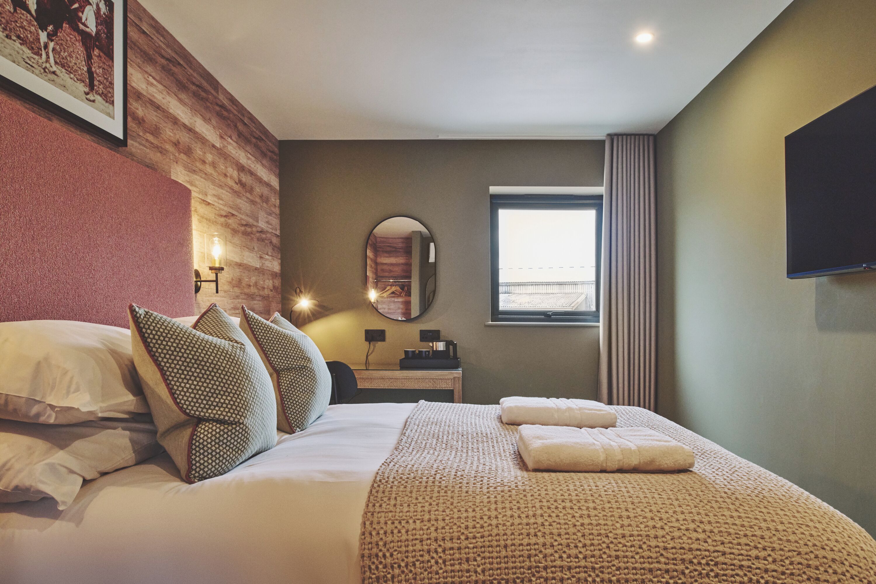 Habitación de hotel con una cama grande, un televisor montado en la pared, una ventana con cortinas y un espejo en la pared.