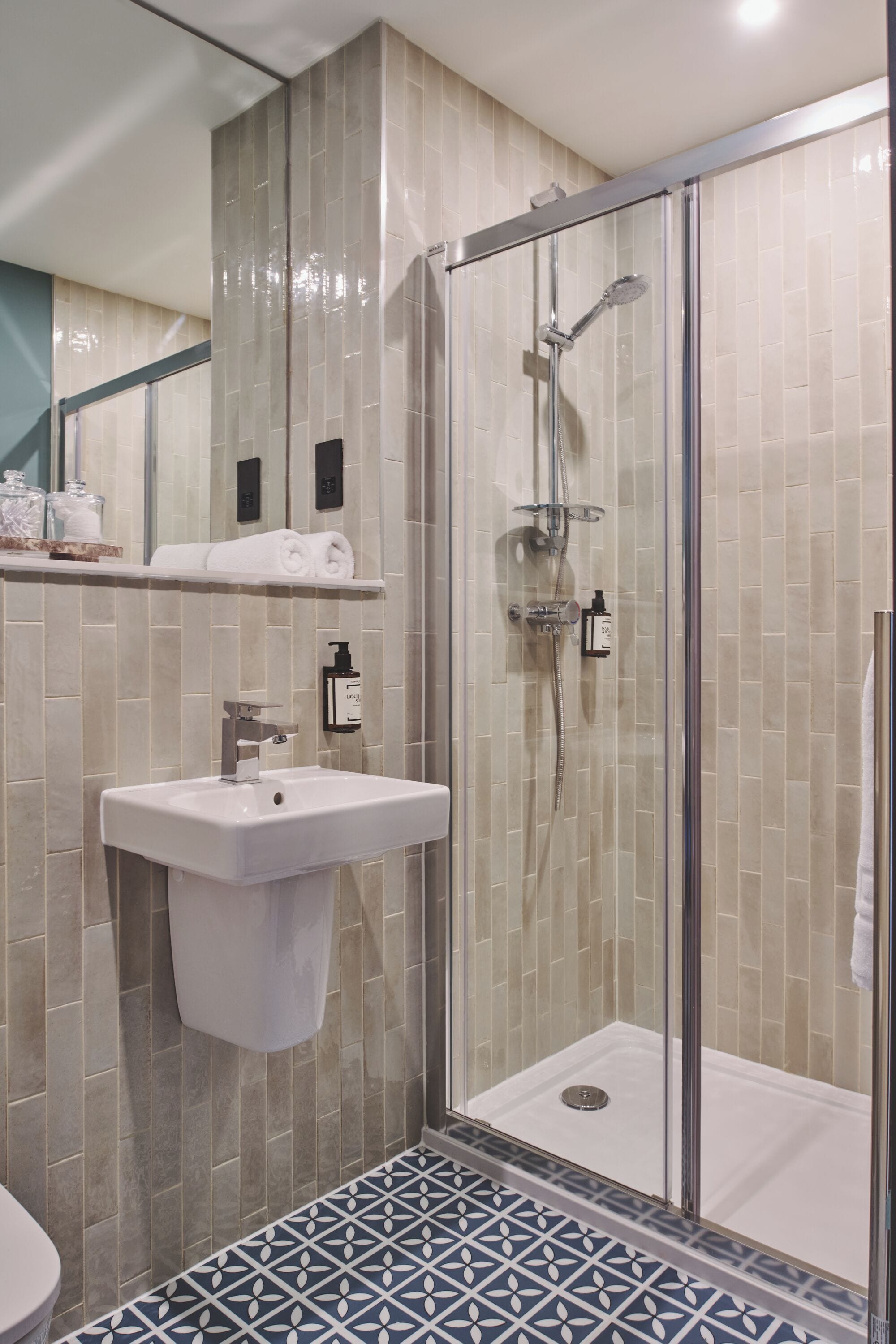 A modern bathroom with a glass-enclosed shower, a sink with a soap dispenser, and a patterned floor.