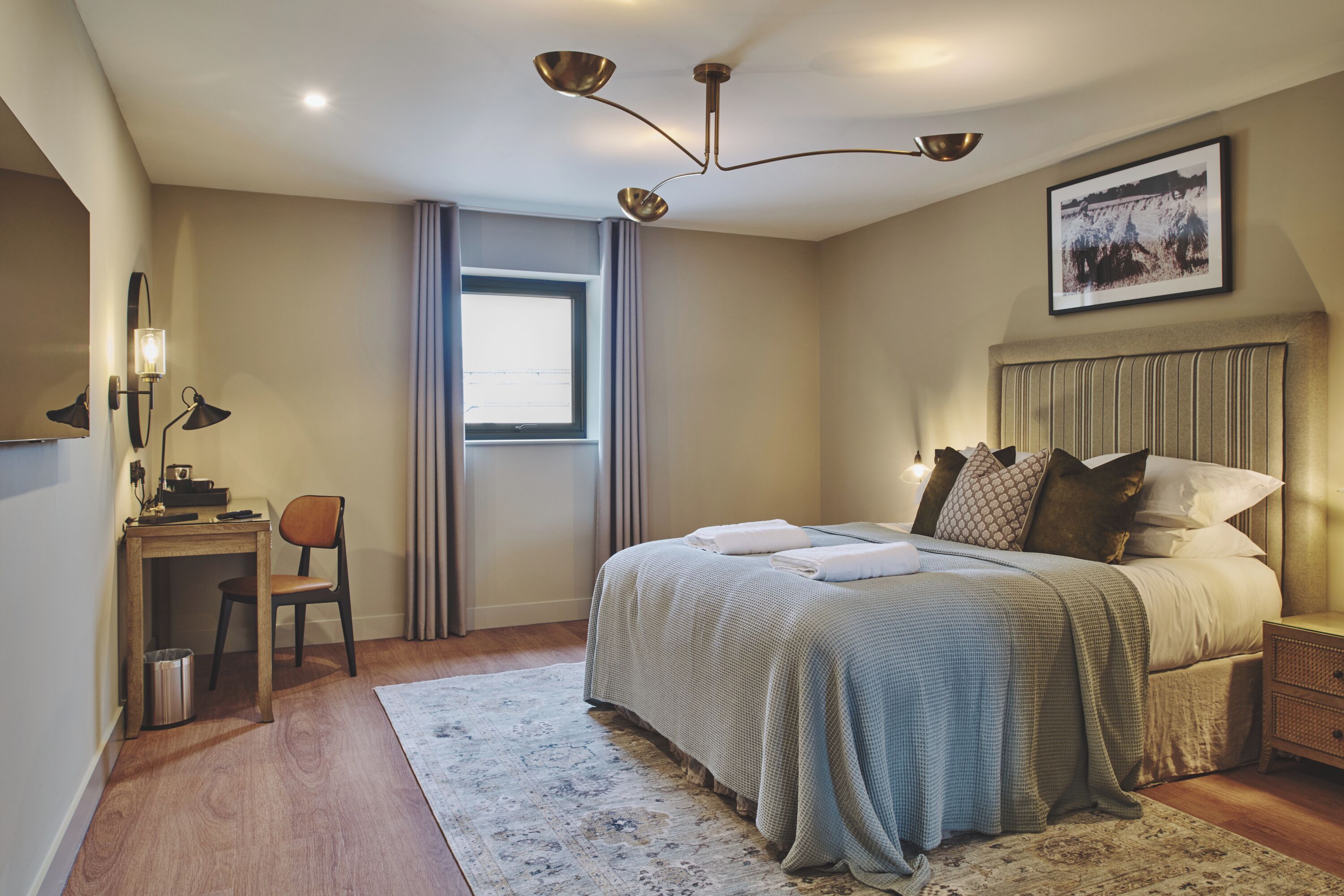 Un dormitorio con cama, mesita de noche, lámpara, silla y ventana con cortinas.