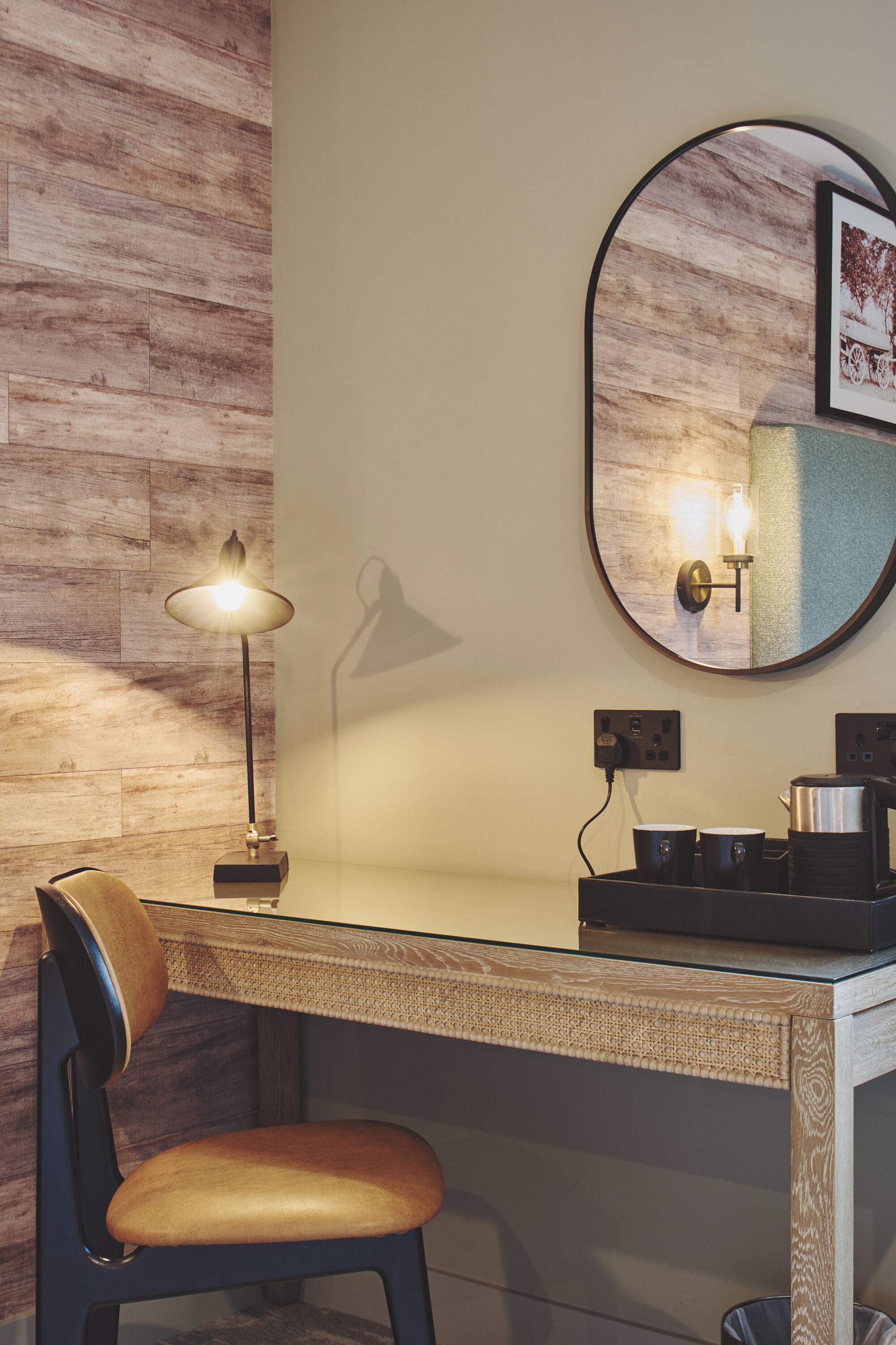 Una habitación moderna con una pared de madera, un espejo redondo, un escritorio con una lámpara y una silla.