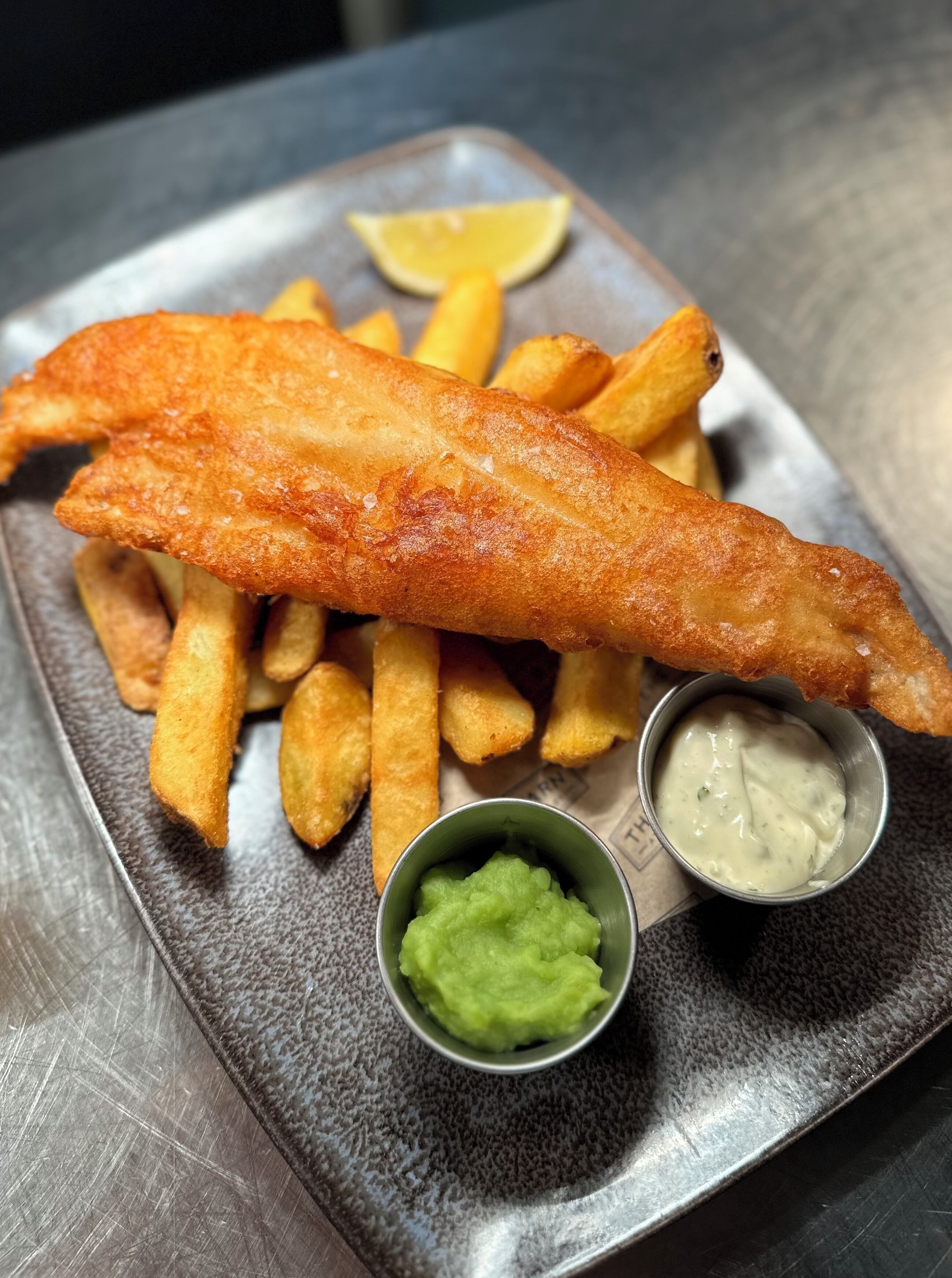 A plate of fish and chips with lemon wedges and two dipping sauces.