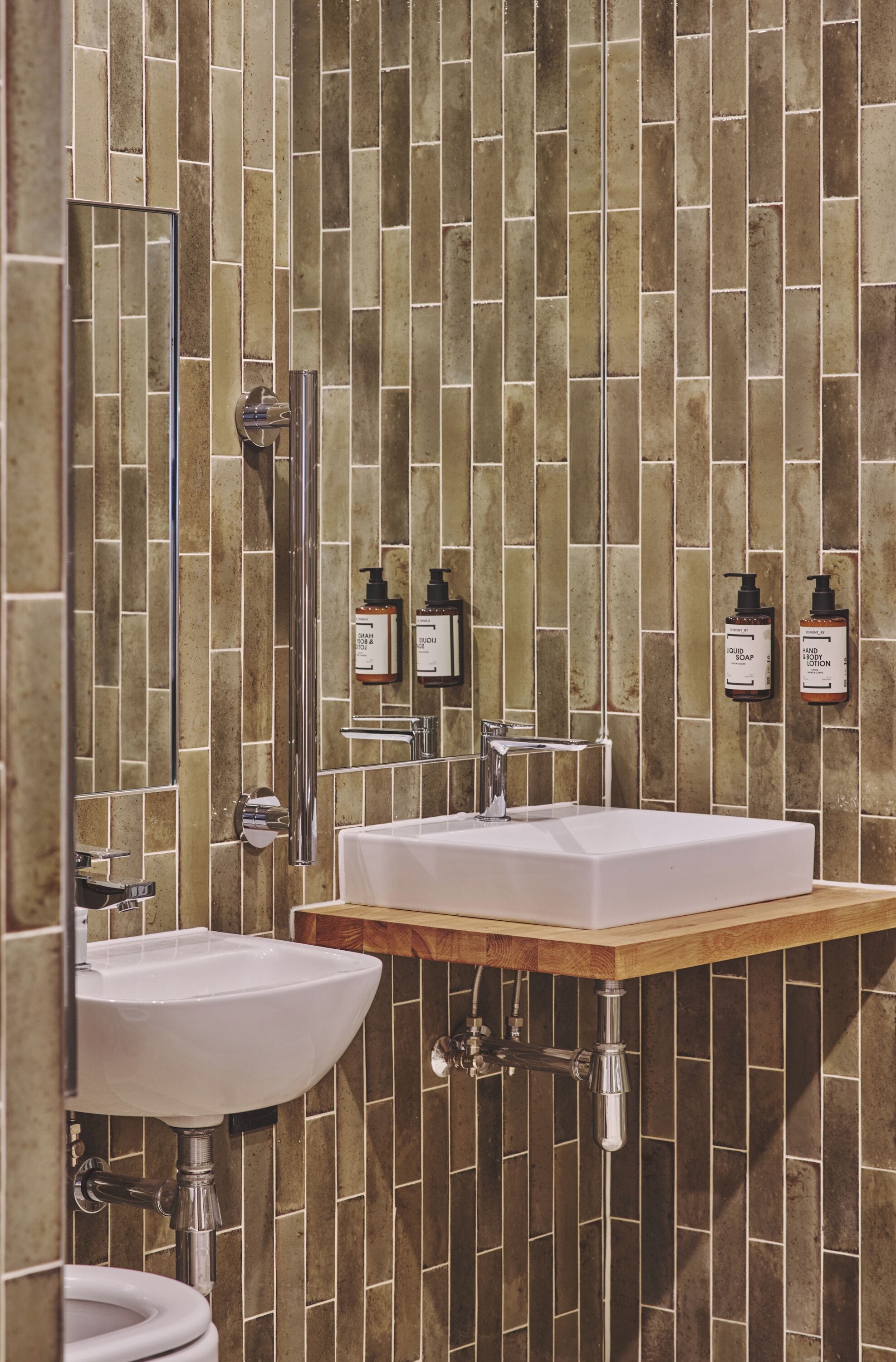 Casa de banho com duas pias, um espelho e produtos de higiene pessoal na parede.