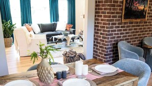 Un comedor con una mesa de madera preparada para cuatro personas, rodeada de sillas grises tapizadas. Una pared de ladrillo con un cuadro enmarcado cuelga sobre la mesa.