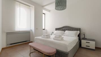 A bedroom with a bed, bedside tables, a bench, and a hanging light fixture.