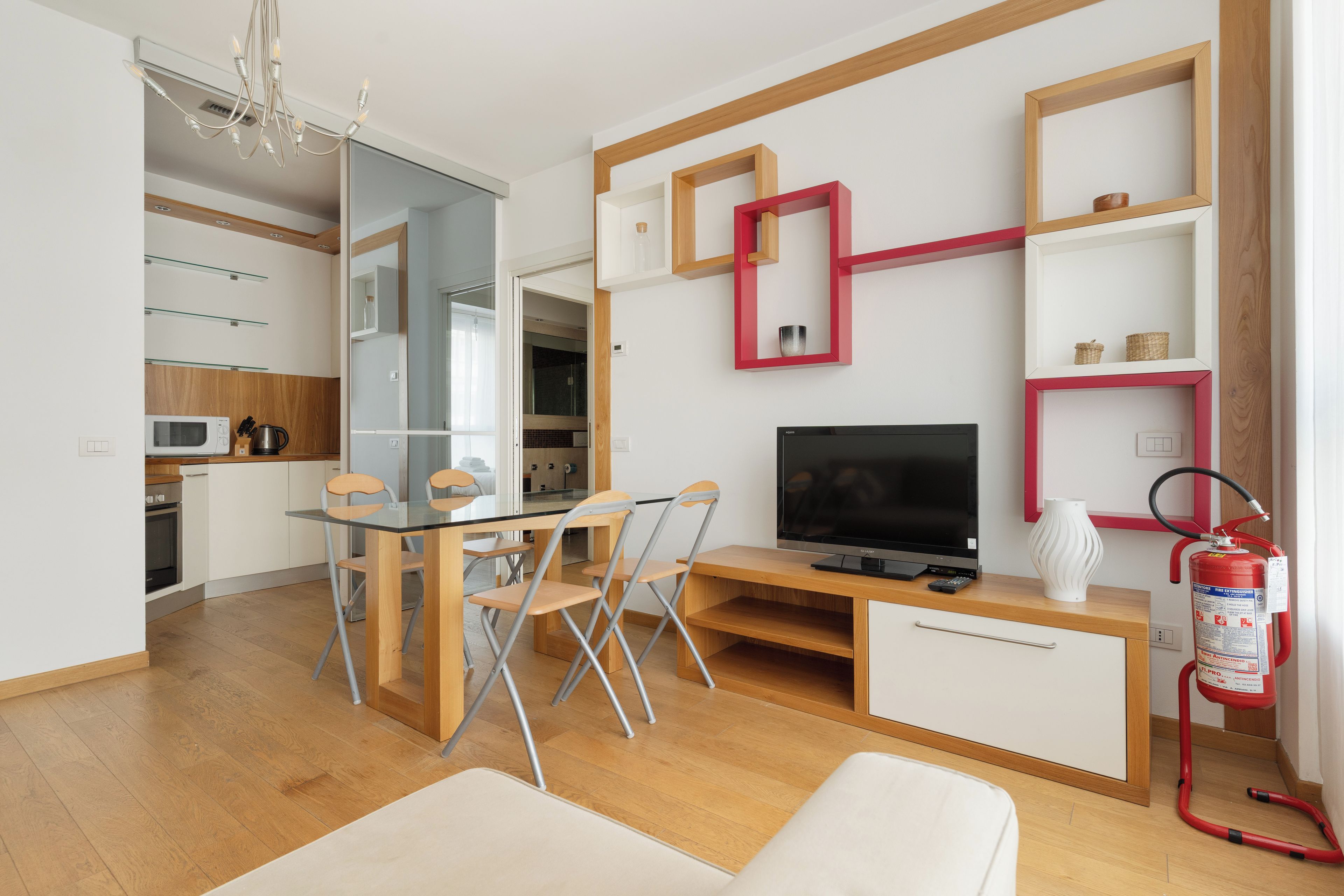 A modern living room with a flat-screen TV, a dining table with chairs, a fireplace, and a kitchen area with a microwave.