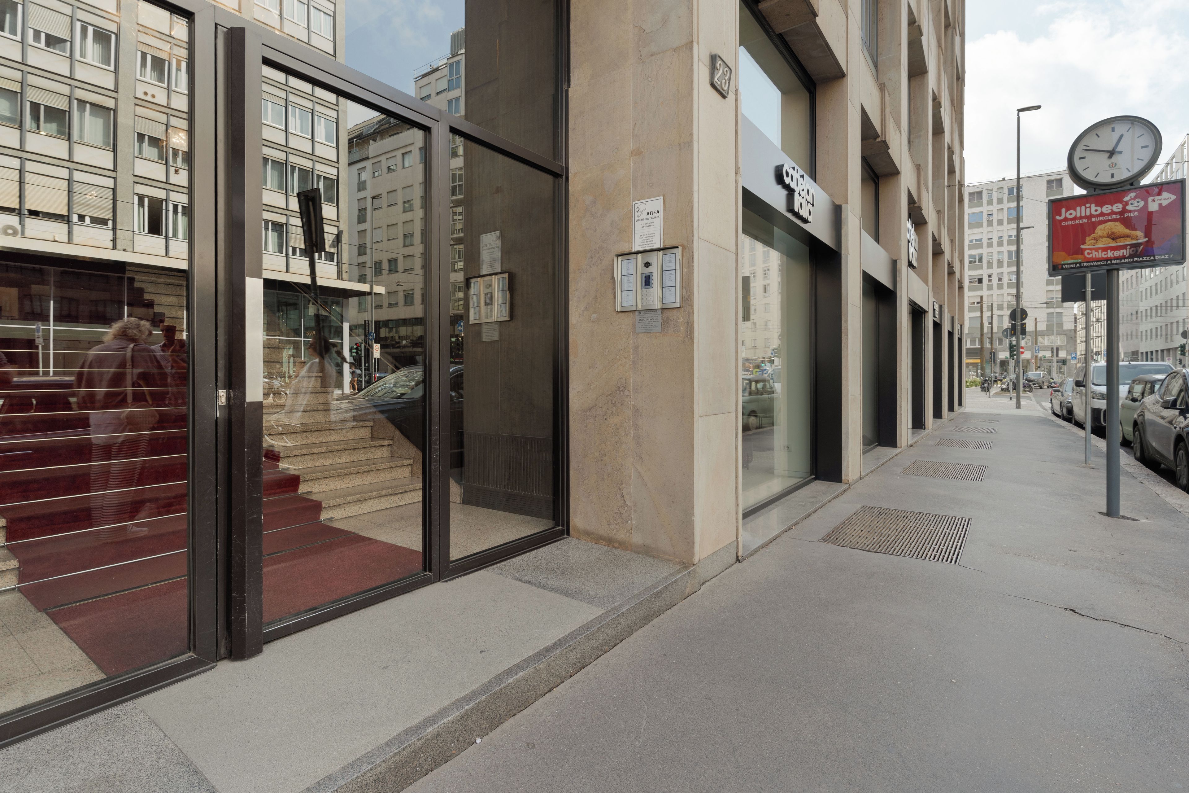 Un edificio moderno con entrada de vidrio, una escalera visible y un reloj en la fachada.