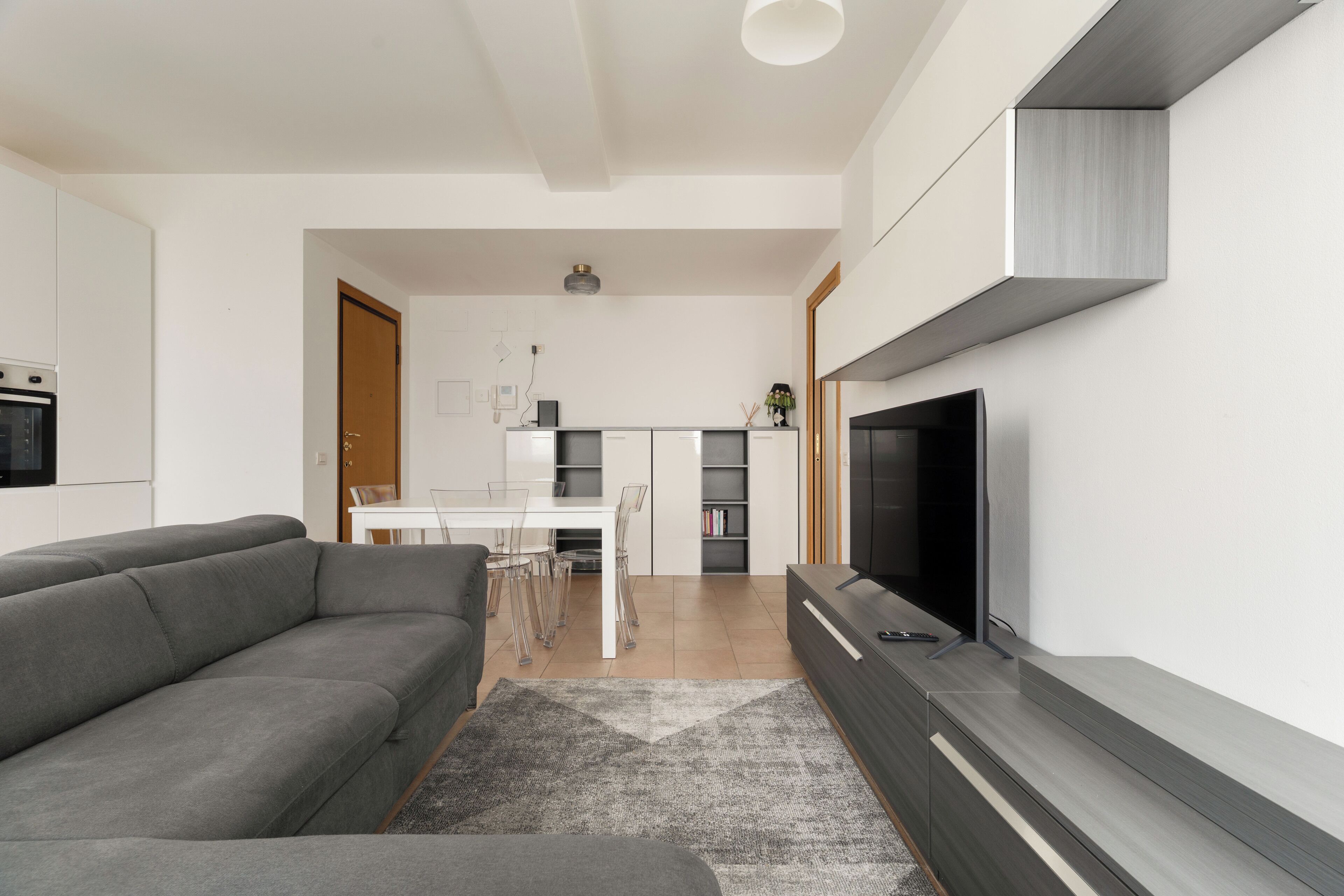 Una sala de estar moderna con un sofá gris, un televisor de pantalla plana y un comedor con una mesa y sillas blancas.