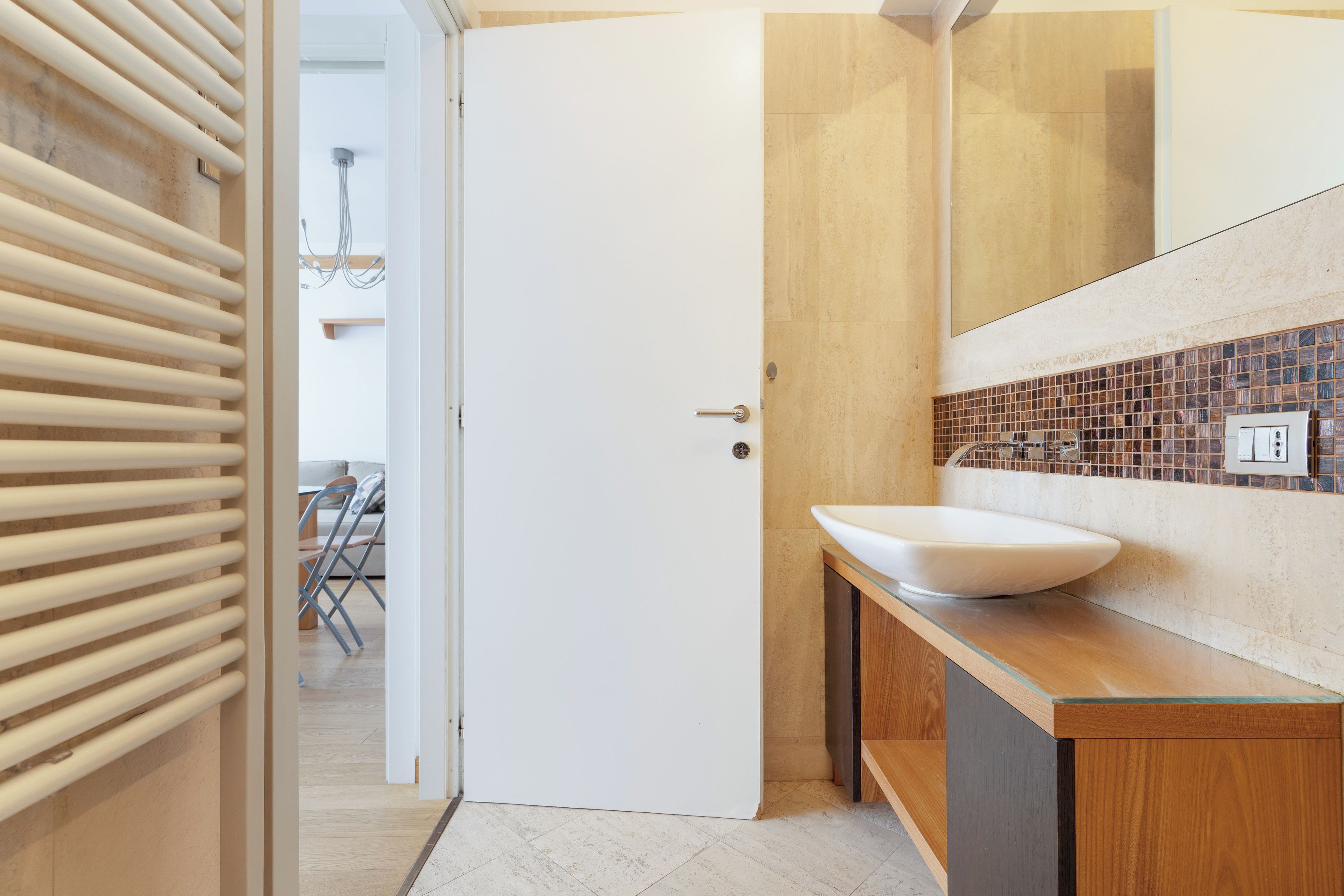 A modern bathroom with a white sink, wooden vanity, and a tiled backsplash.
