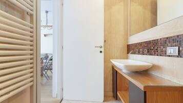 A modern bathroom with a white sink, wooden vanity, and a tiled backsplash.