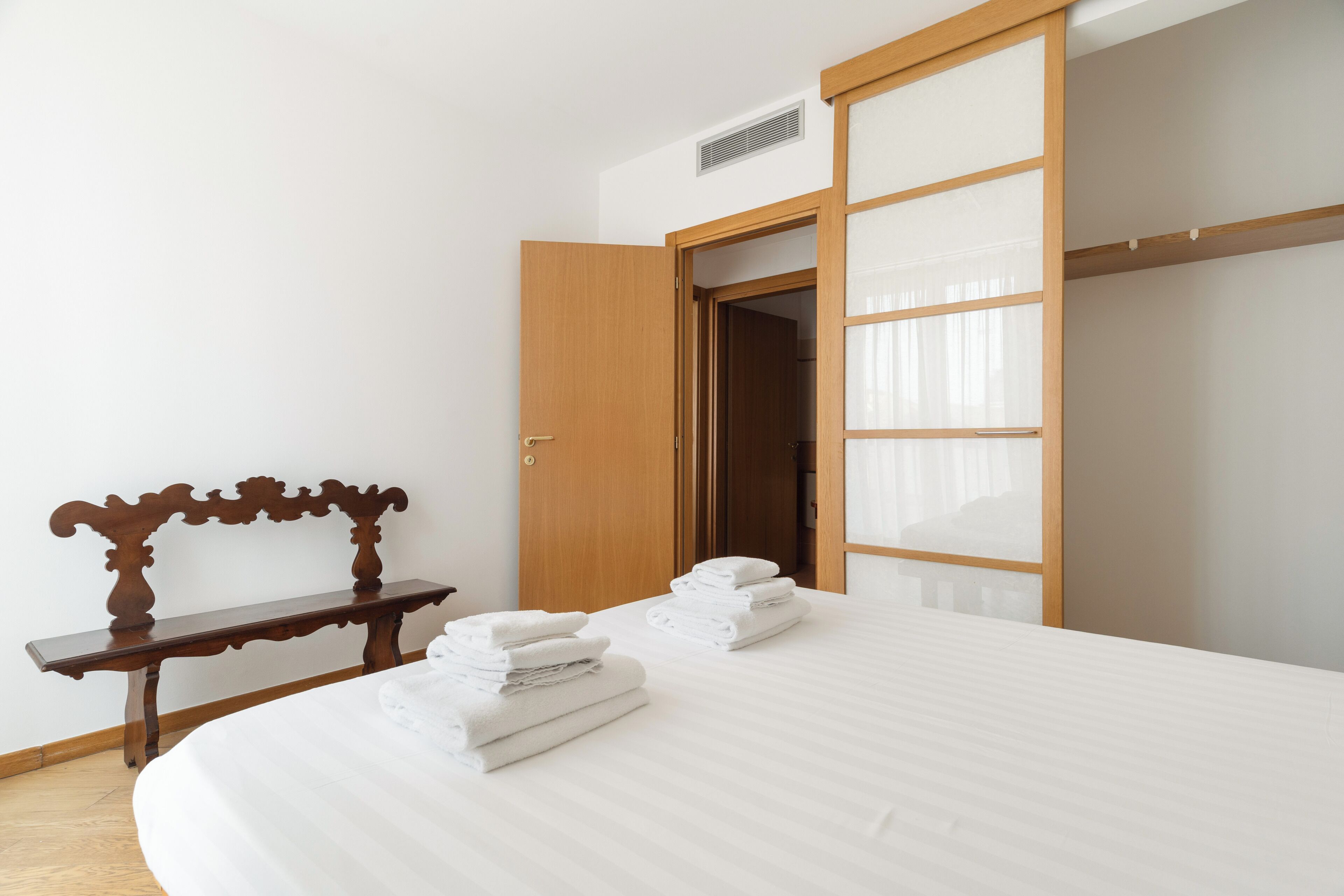 A hotel room with a bed, a bench, a wardrobe, and a door.