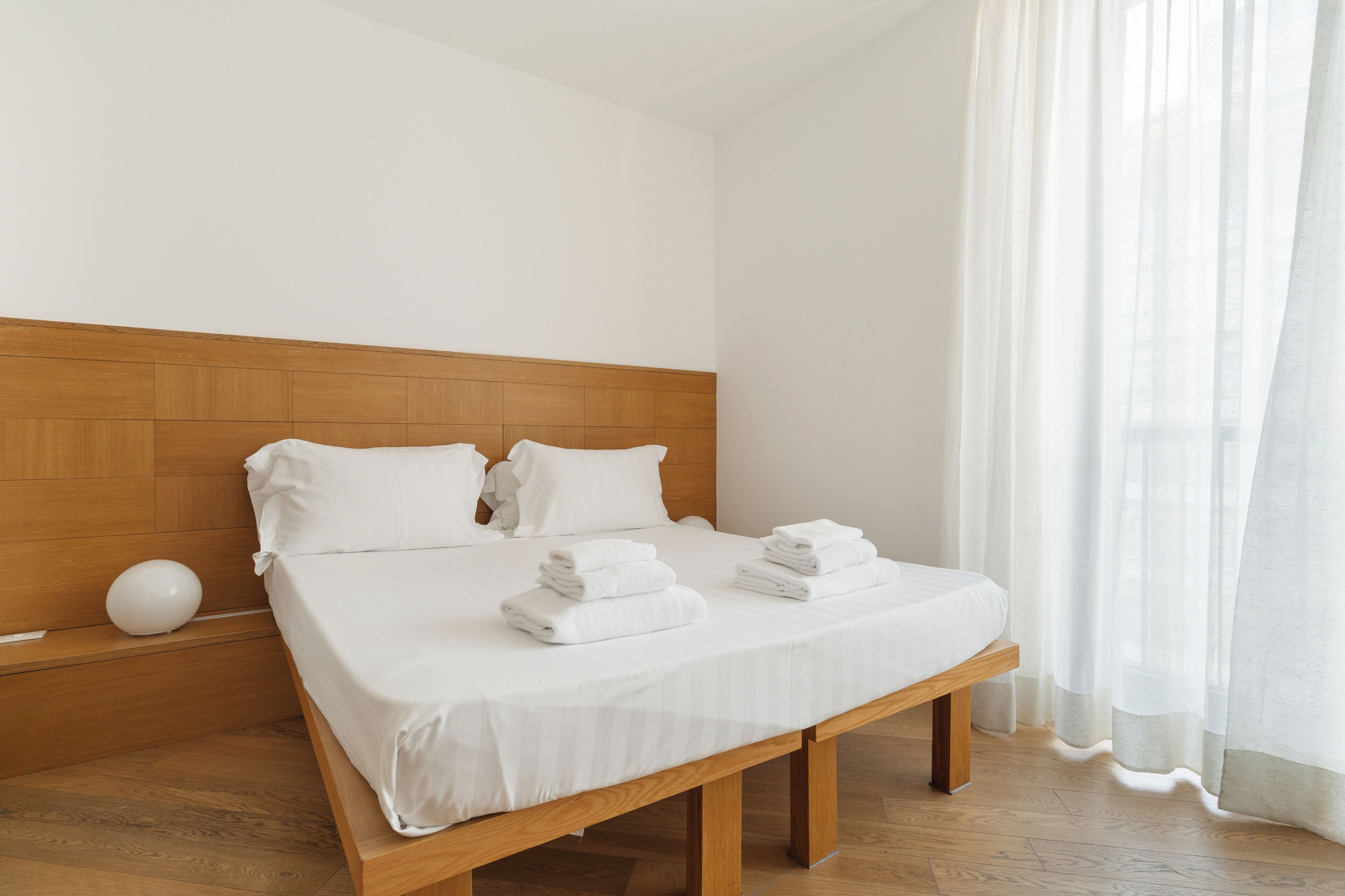 Un lit bien fait, avec du linge de lit et des serviettes blanches, une tête de lit en bois et un plancher en bois.