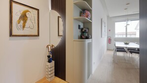 Ein modernes Interieur mit einer weißen Wand, einem gerahmten Kunstwerk, einer Holztrennwand, einem weißen Schrank mit Dekoration und einem Essbereich mit Tisch und Stühlen.