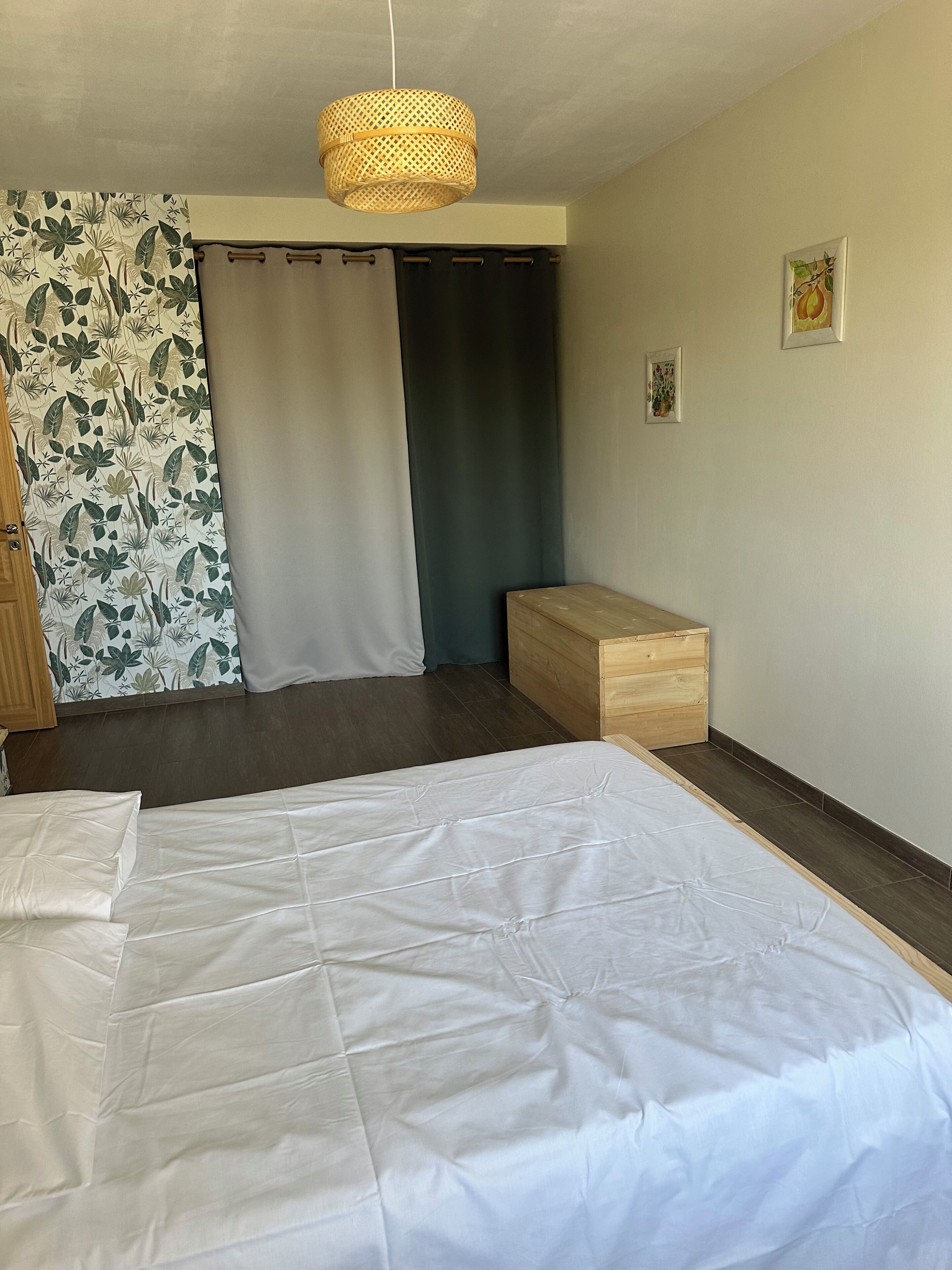 Un dormitorio con cama, un banco de madera, una lámpara colgante y una puerta con cortinas.