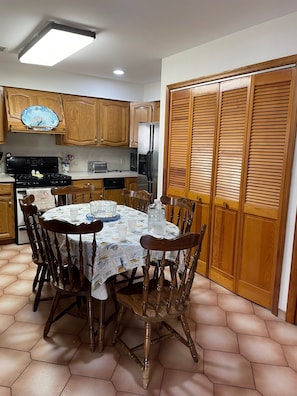 Een keuken met houten kastjes, een koelkast, een fornuis en een eettafel met stoelen.