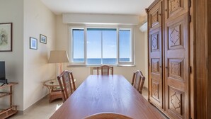 A dining area with a long wooden table, chairs, a lamp, and a view of the sea through a large window. - The Sound of the Sea by Wonderful Italy (Sanremo)