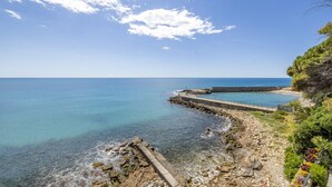 A coastal landscape with a clear sky, rocky shore, and a concrete sea wall. - The Sound of the Sea by Wonderful Italy (Sanremo)