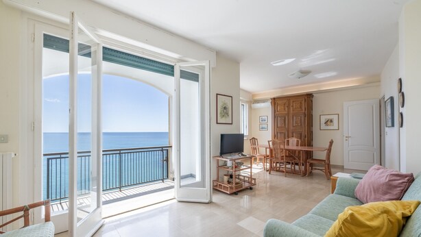 A spacious living area with a balcony overlooking the sea, a dining area with wooden furniture, and a cozy seating area with cushions. - The Sound of the Sea by Wonderful Italy (Sanremo)