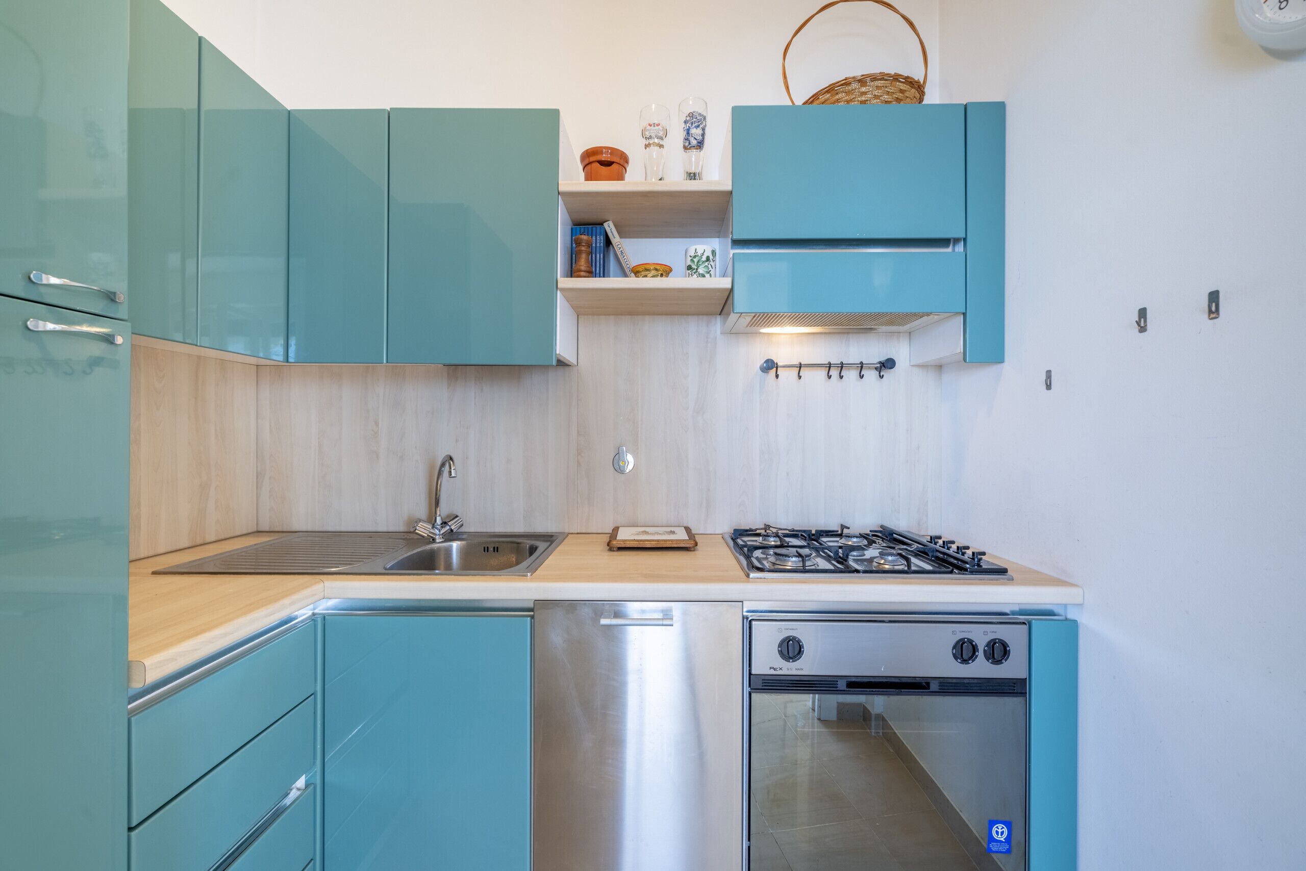 A compact kitchen with teal cabinetry, a stainless steel dishwasher, and a built-in oven.