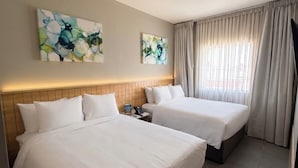 A hotel room with two beds, a nightstand, and a window with curtains.
