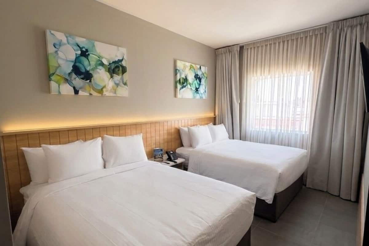 A hotel room with two beds, a nightstand, and a window with curtains.