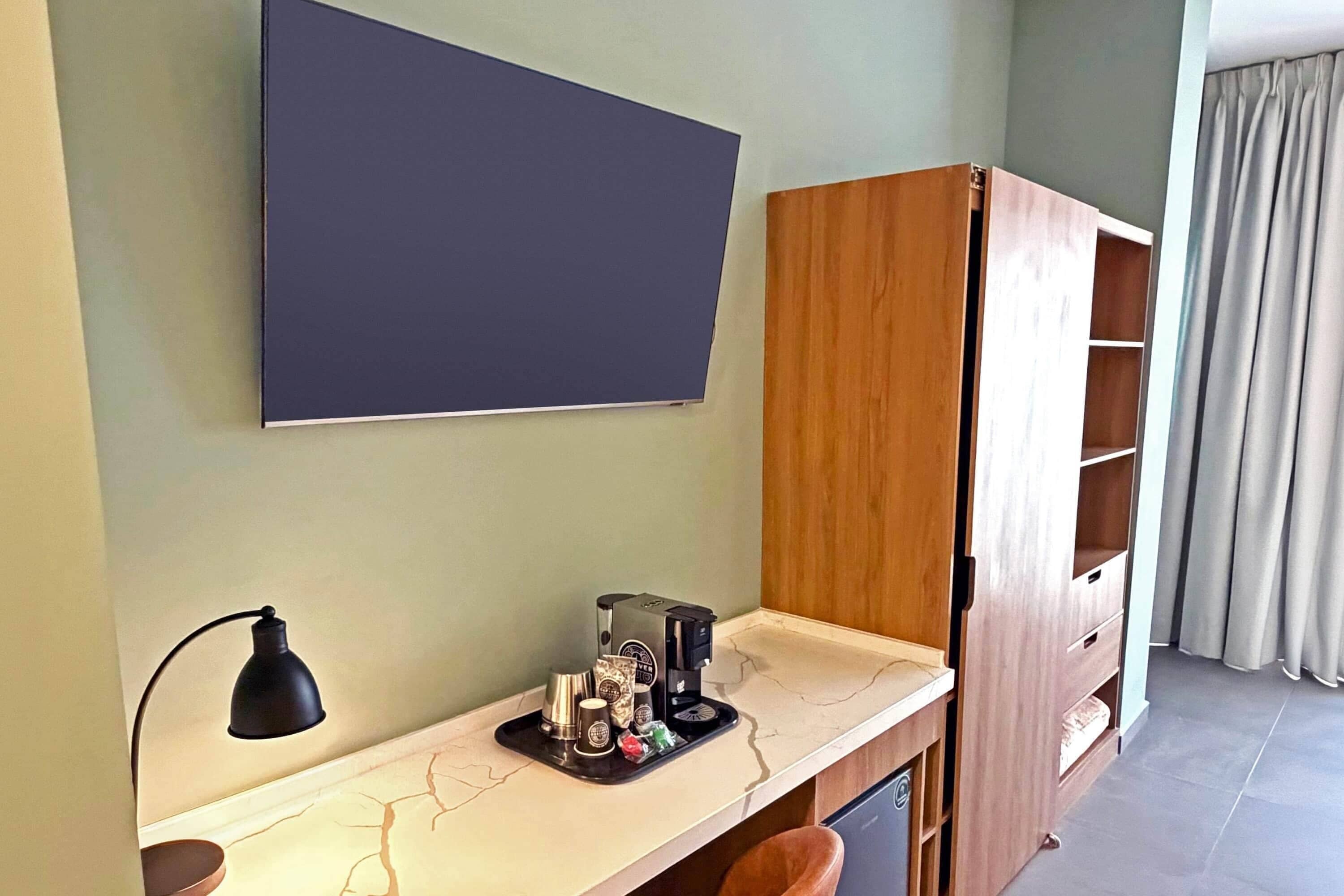 A room with a desk, a lamp, a coffee maker, and a wardrobe.