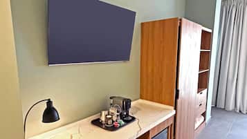 A room with a desk, a lamp, a coffee maker, and a wardrobe.