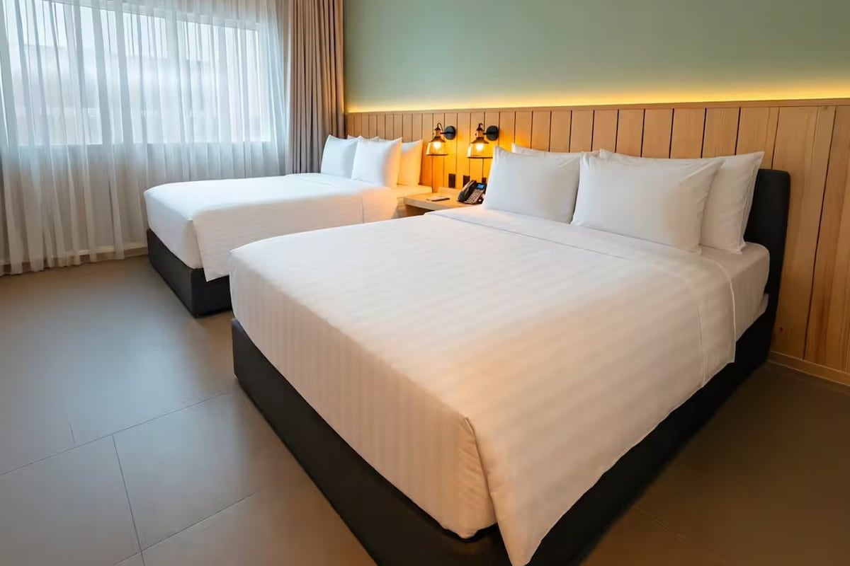 A hotel room with two beds, a bedside table with a lamp, and a phone.