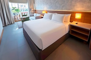 A hotel room with a large bed, bedside tables, a chair, and a view of the outside.