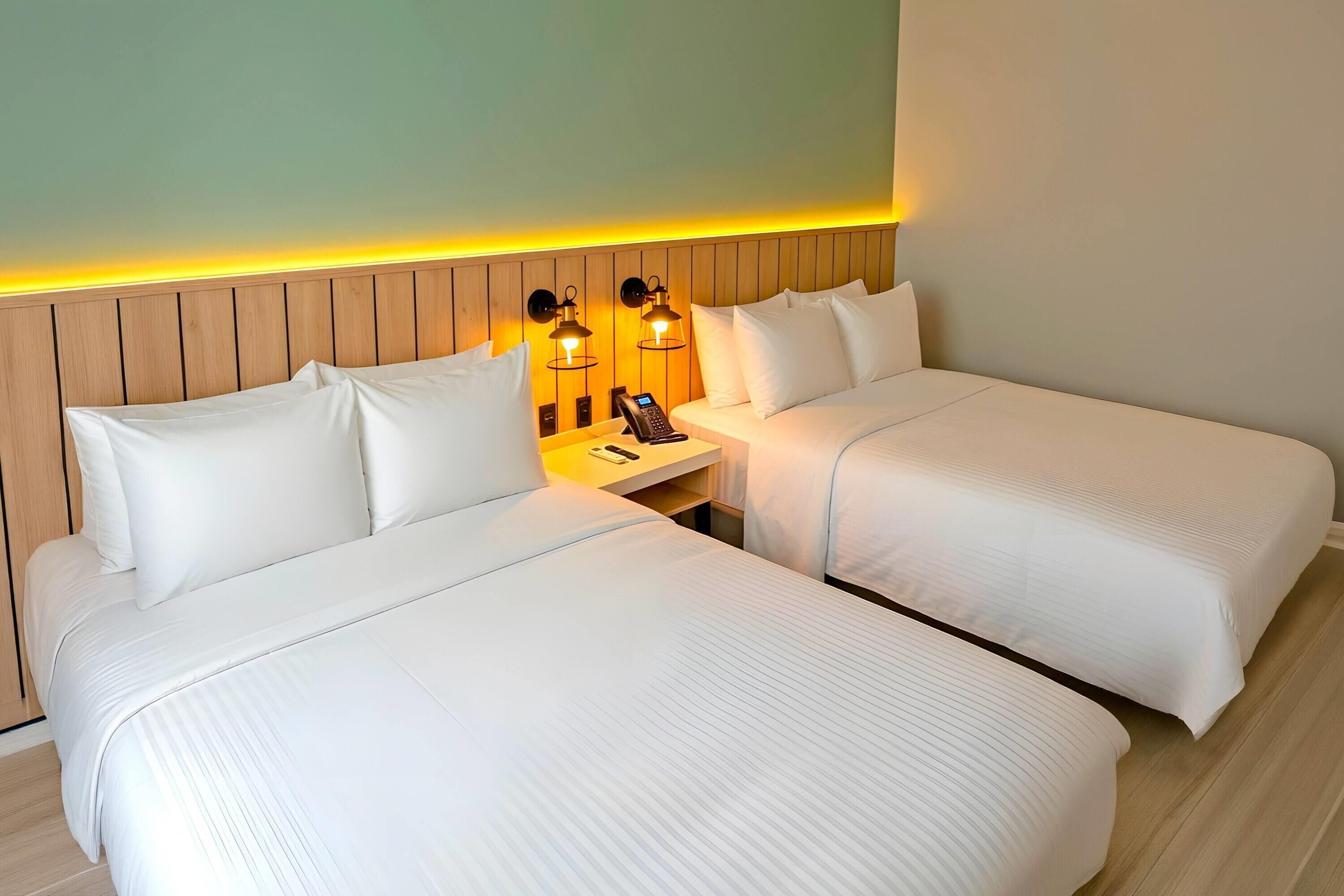 A hotel room with two beds, a wooden headboard, a nightstand with a phone, and wall-mounted lamps.